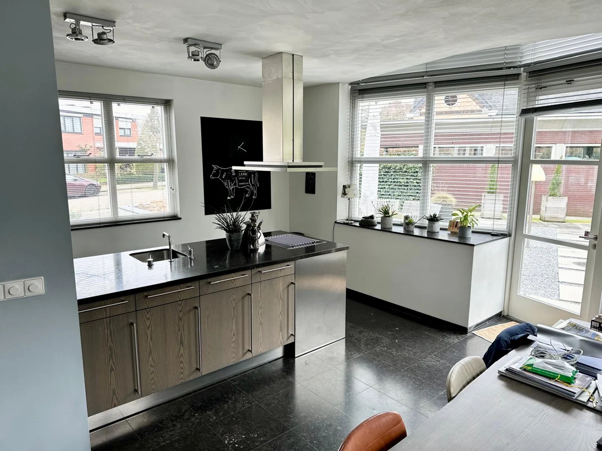 Lichte keuken met een kookeiland, donker werkblad, houtaccenten en grote ramen